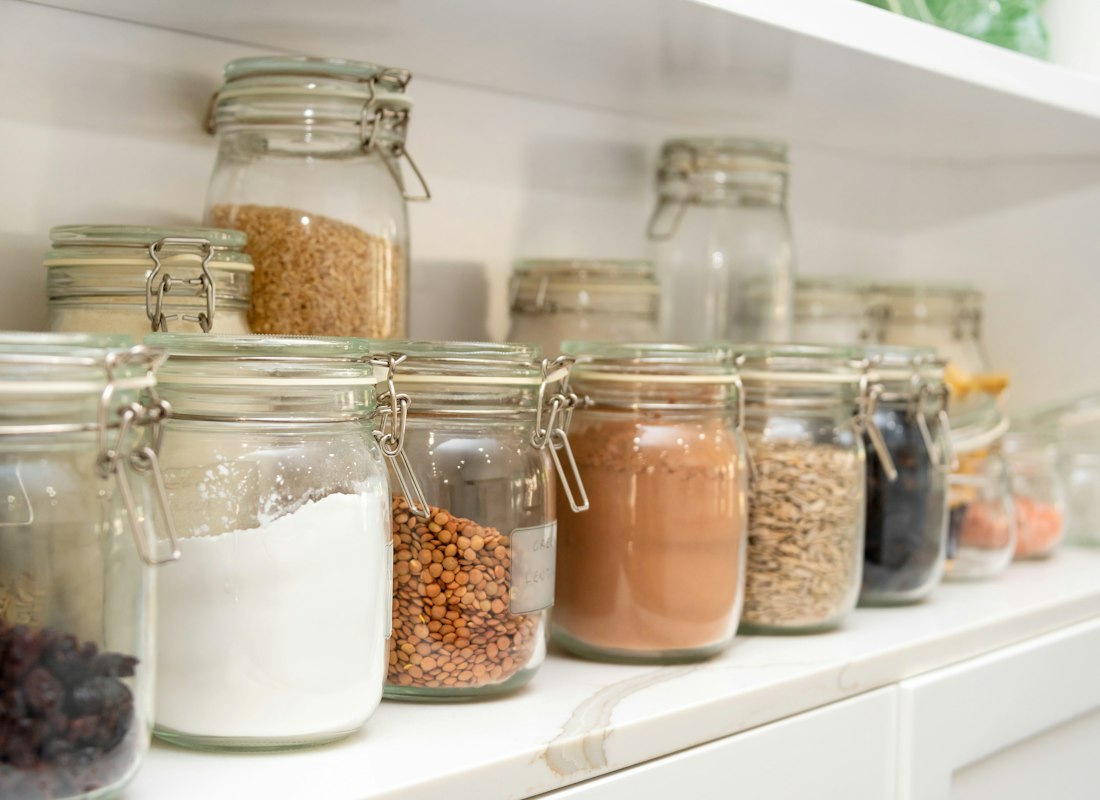 Glass clamp-top jars of flour, grains and pulses on a white shelf